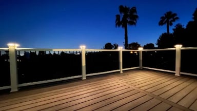 A beautifully illuminated deck at dusk surrounded by palm trees.
